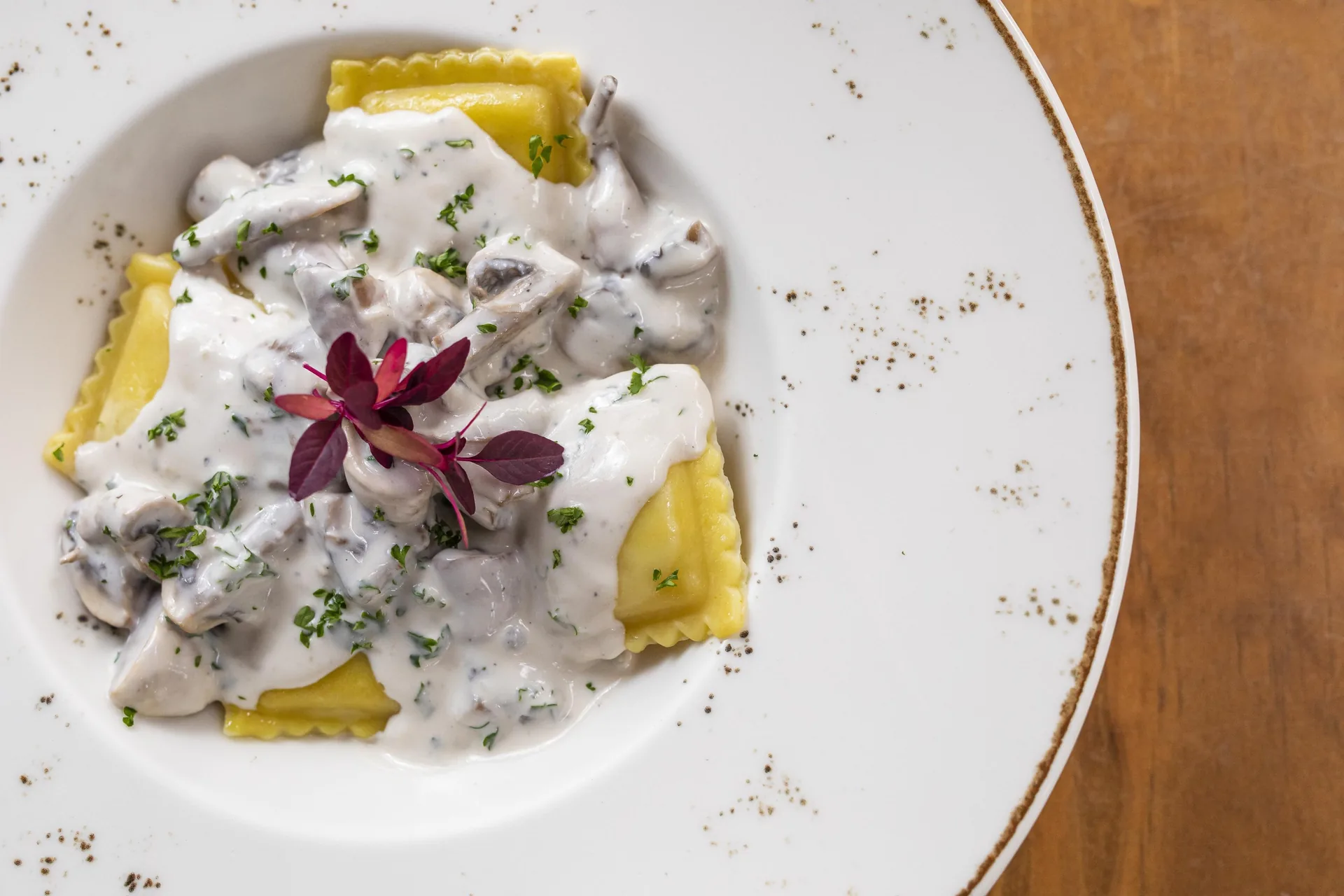 Raviolis en salsa blanca con champiñones laminados y perejil picado, en un plato hondo blanco.