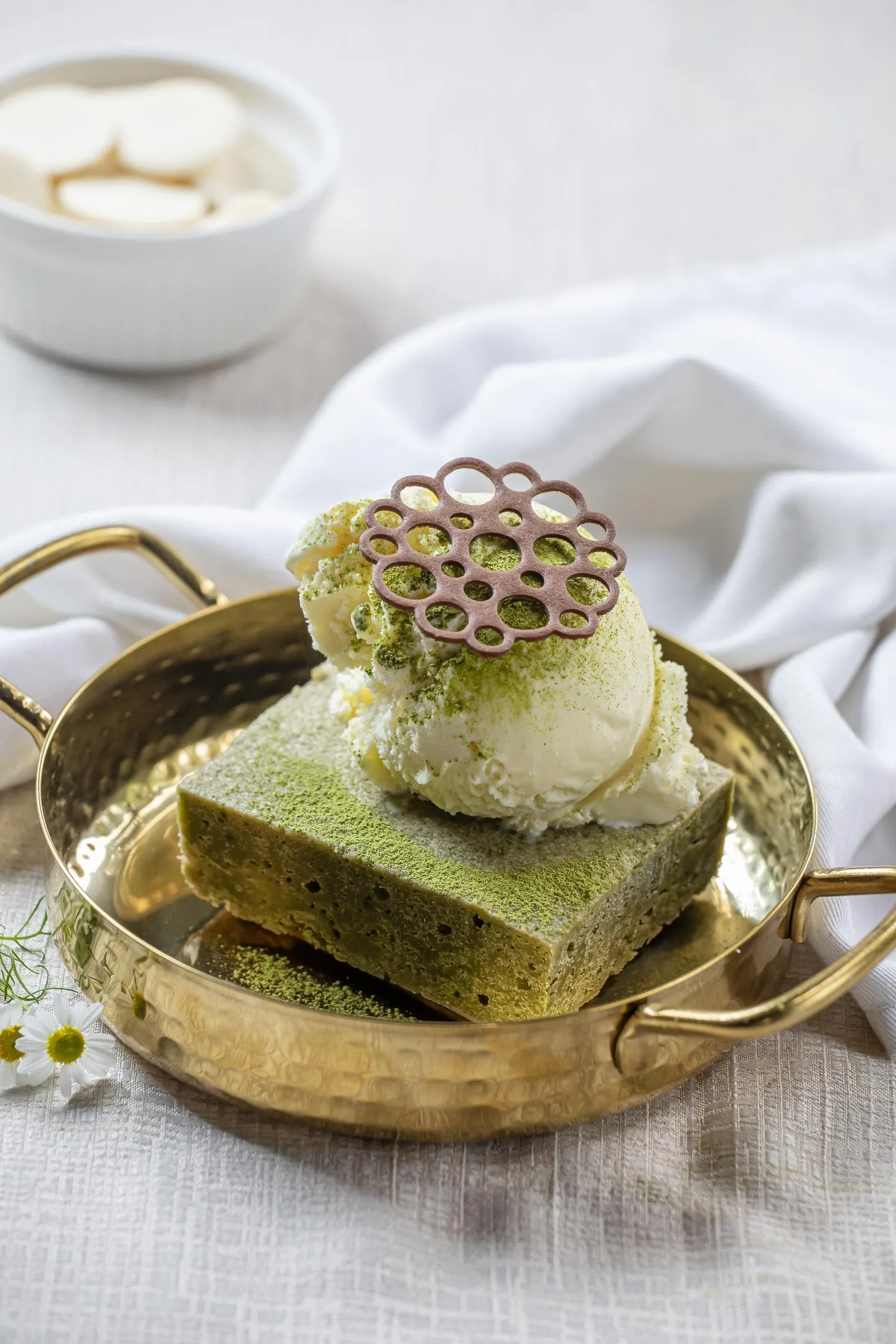 Porción de bizcocho verde con una bola de helado y un disco calado de chocolate encima, servida en una bandeja dorada.
