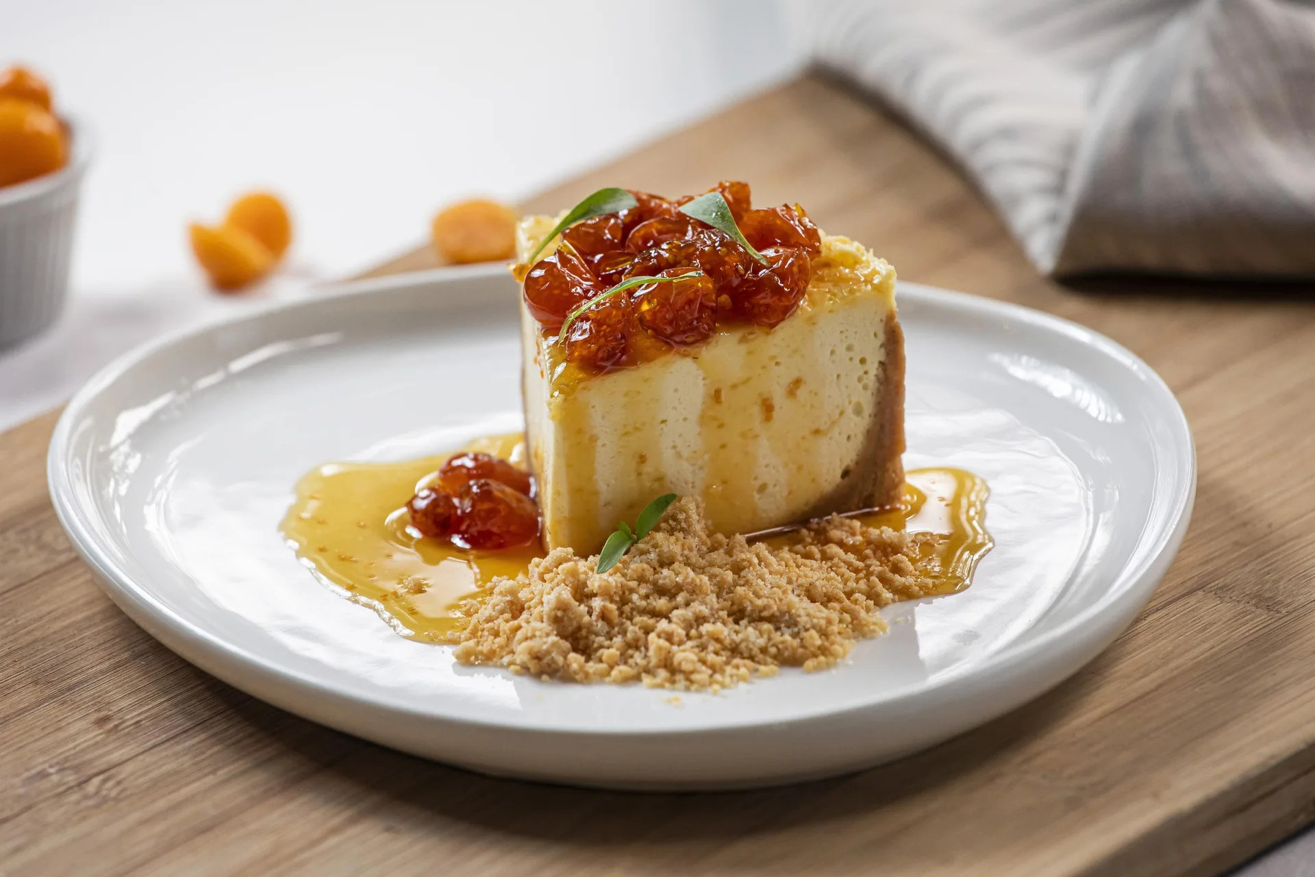 Porción de tarta de queso con compota de fruta por encima, servida sobre migas de galleta y un hilo de almíbar.