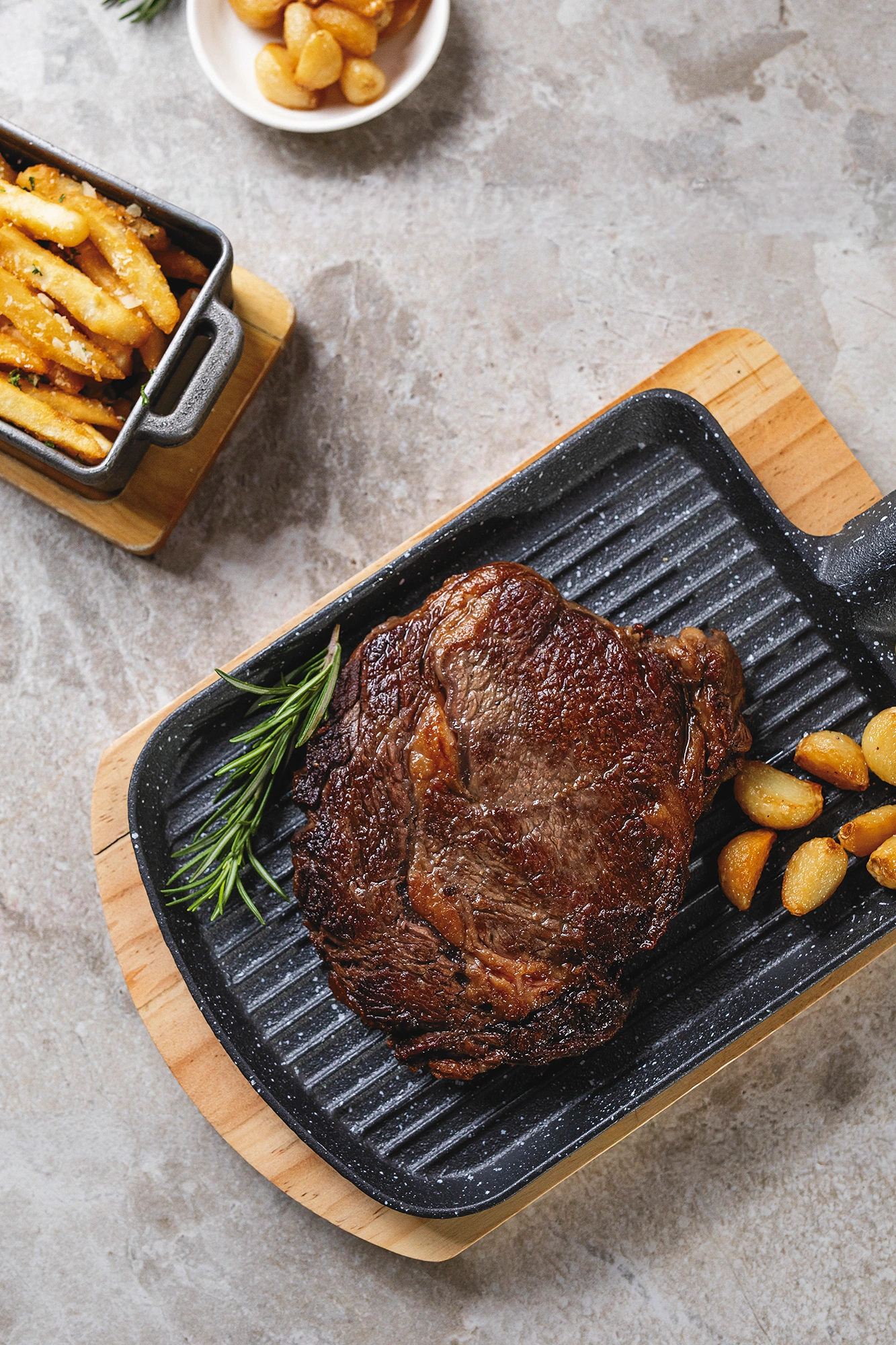 Corte rib eye a la parrilla en una plancha de hierro sobre tabla de madera, con papas doradas al lado