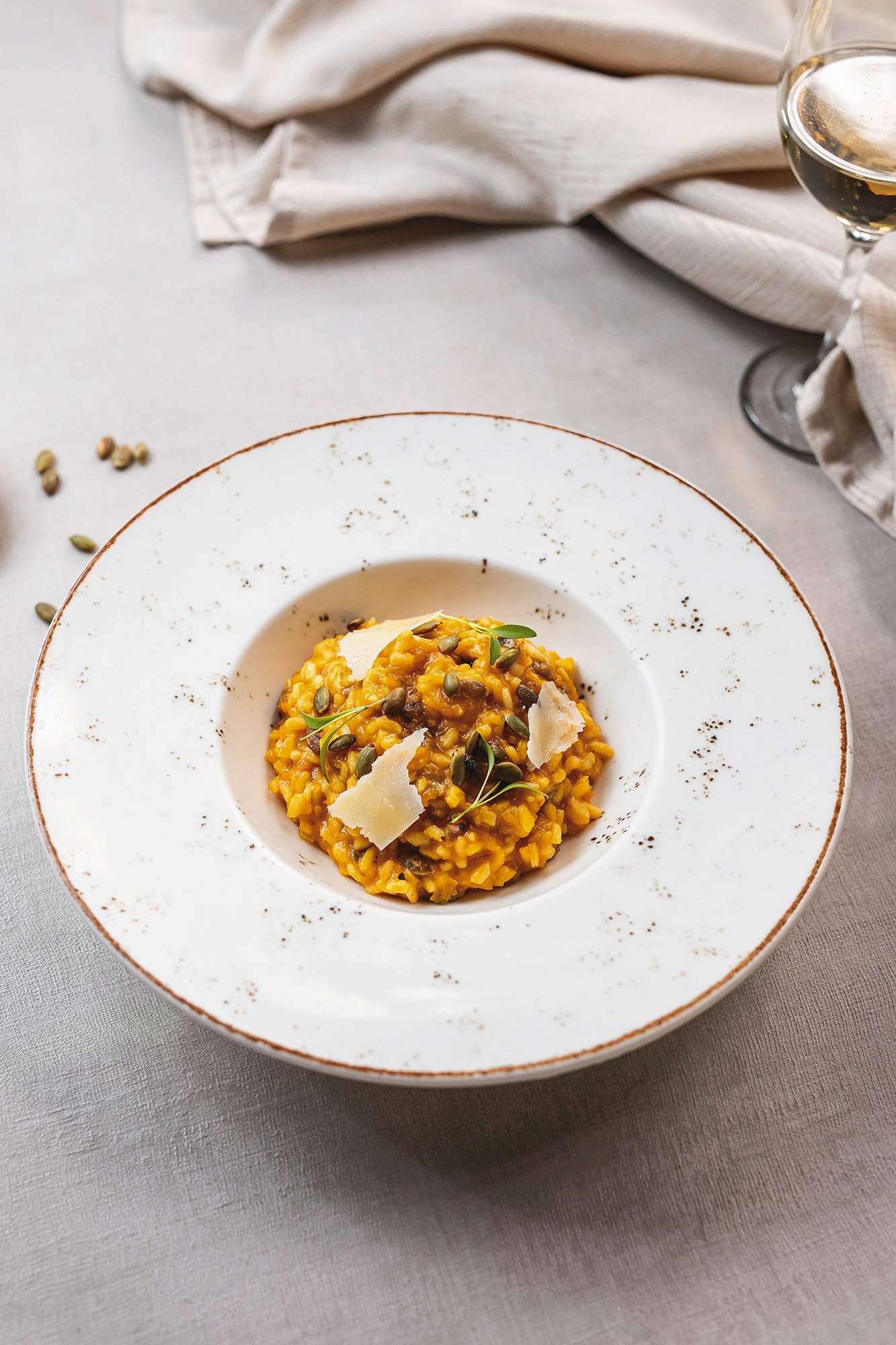 Risotto de color anaranjado con láminas de queso y brotes verdes, en un plato hondo de borde moteado