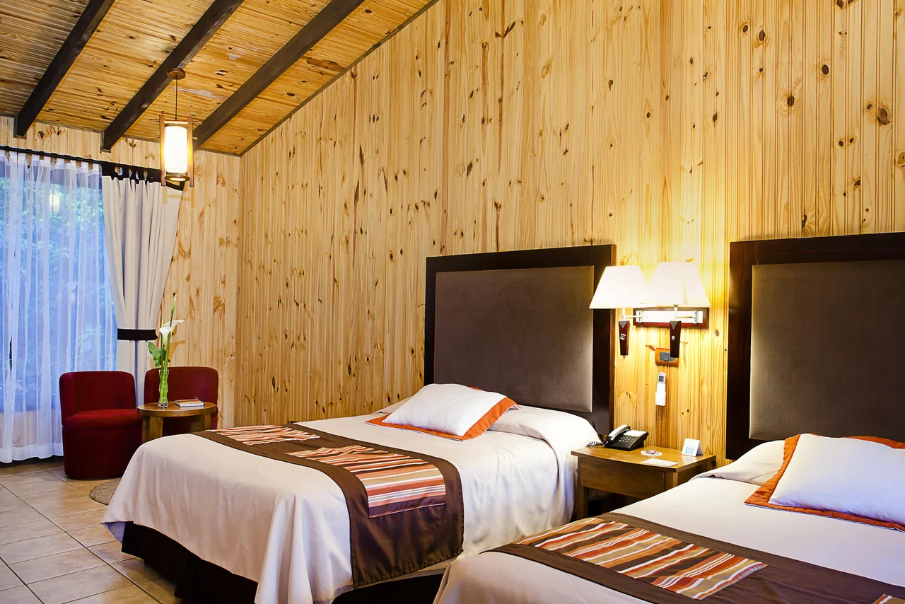 Habitación Estándar con dos camas matrimoniales y la butaca roja junto a la ventana