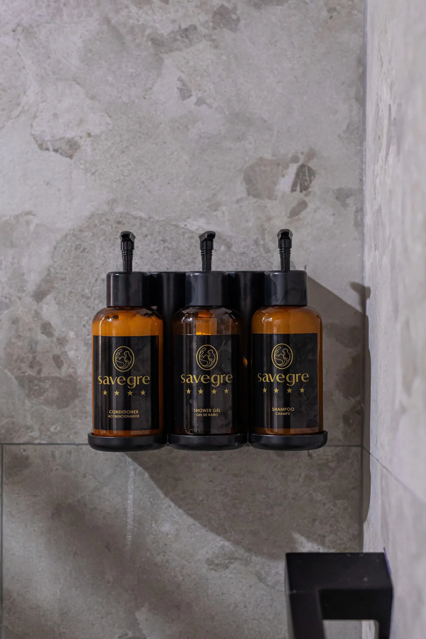 Three Savegre-branded dispensers — conditioner, shower gel and shampoo — mounted on the stone wall of the shower.