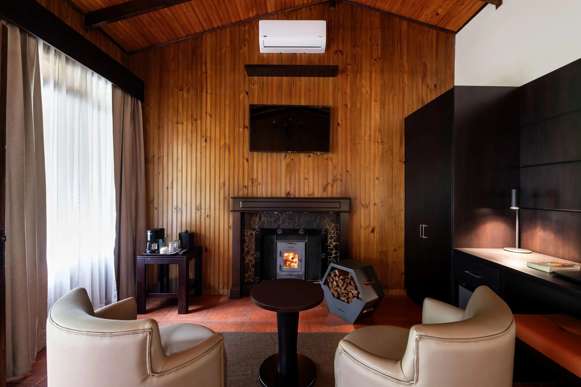 Sala de estar de la Master Suite con chimenea encendida, dos butacas y el televisor sobre la pared de madera