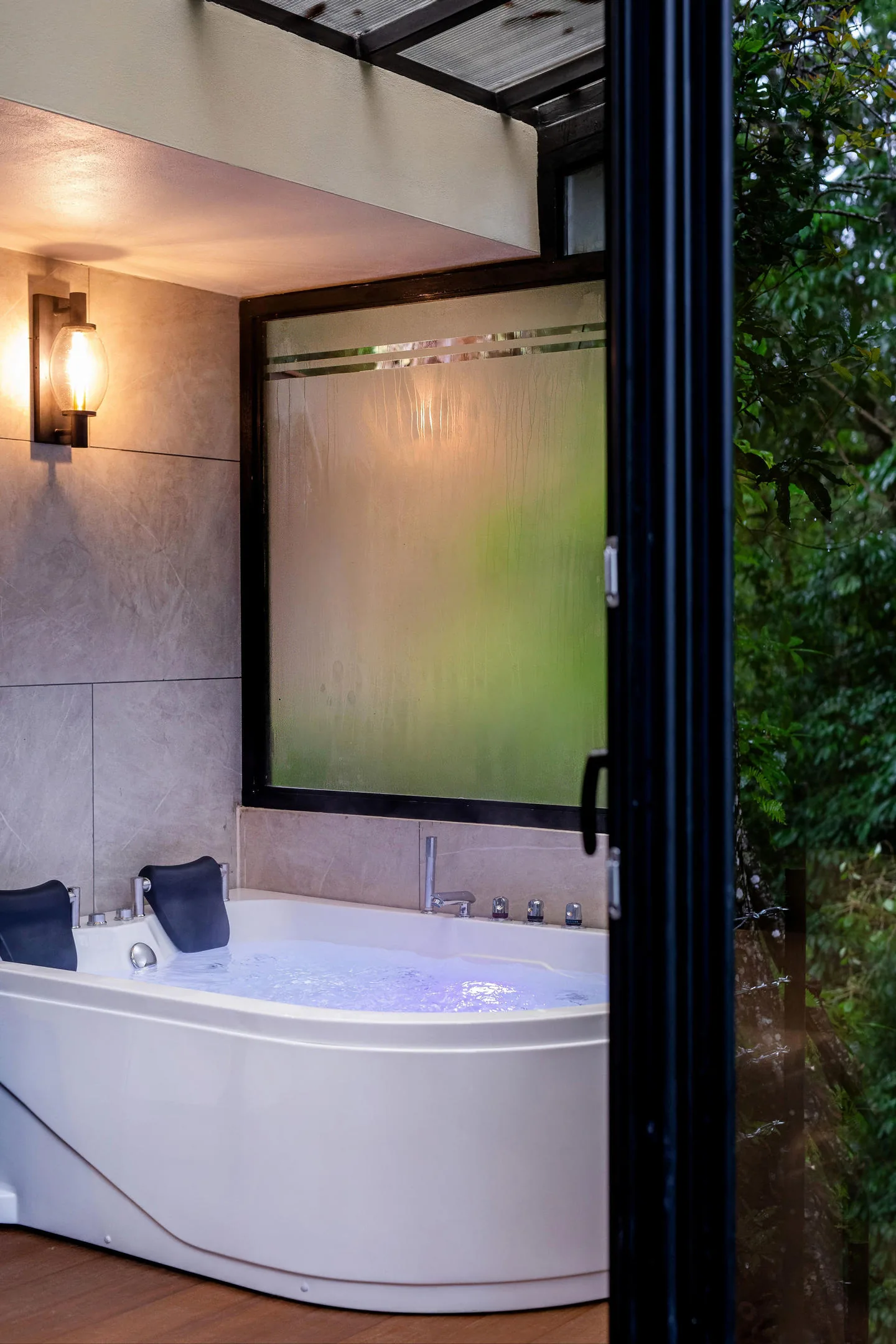 A corner jacuzzi with the water running, beside a frosted window and the stone wall.