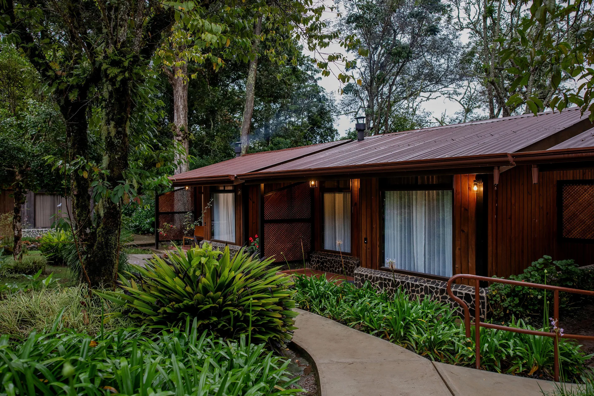 A row of cabins with the terrace lights on at dusk, beside the path and the garden.