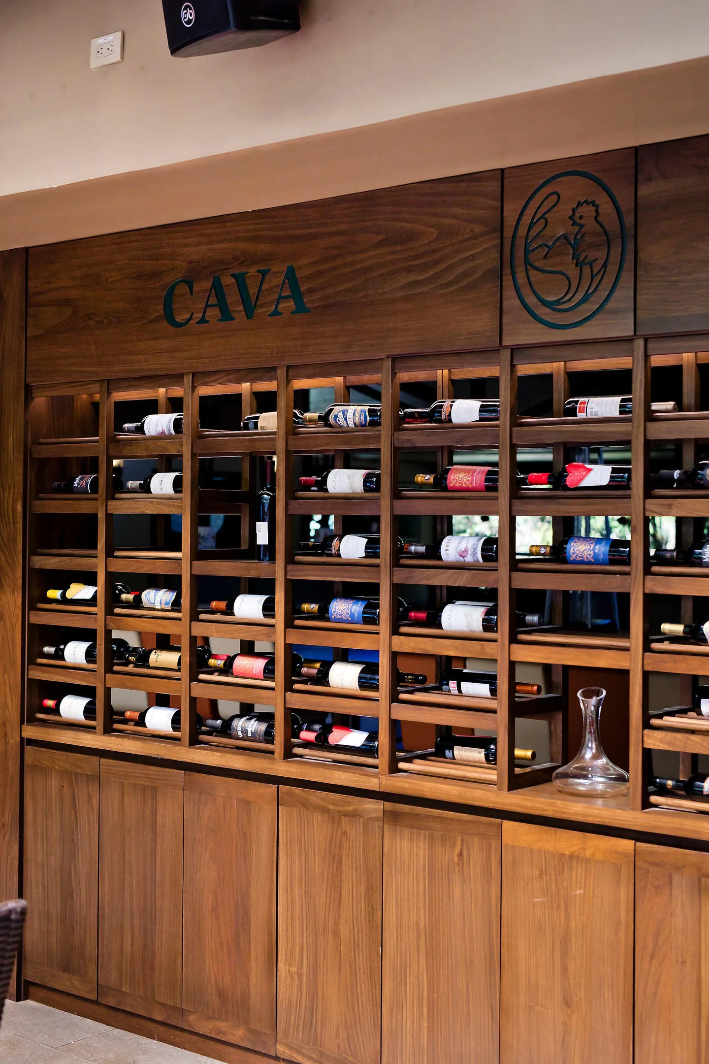 La cava del restaurante: un mueble de madera con las botellas tumbadas en sus casilleros, con la palabra «CAVA» grabada arriba y un decantador de vidrio a la derecha.